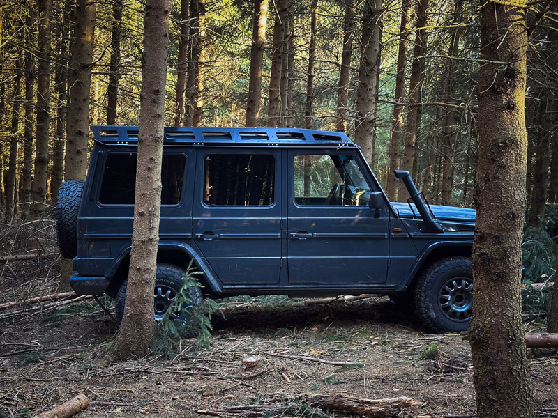 Blaue G-Klasse mit Walger Works Dachtraeger zwischen Baeumen